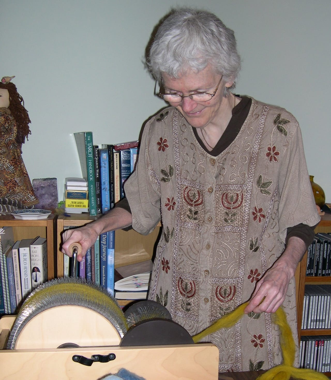 Hands carding wool that has been dyed yellow with marigold flowers, the carder's teeth opening the fiber locks and aligning them