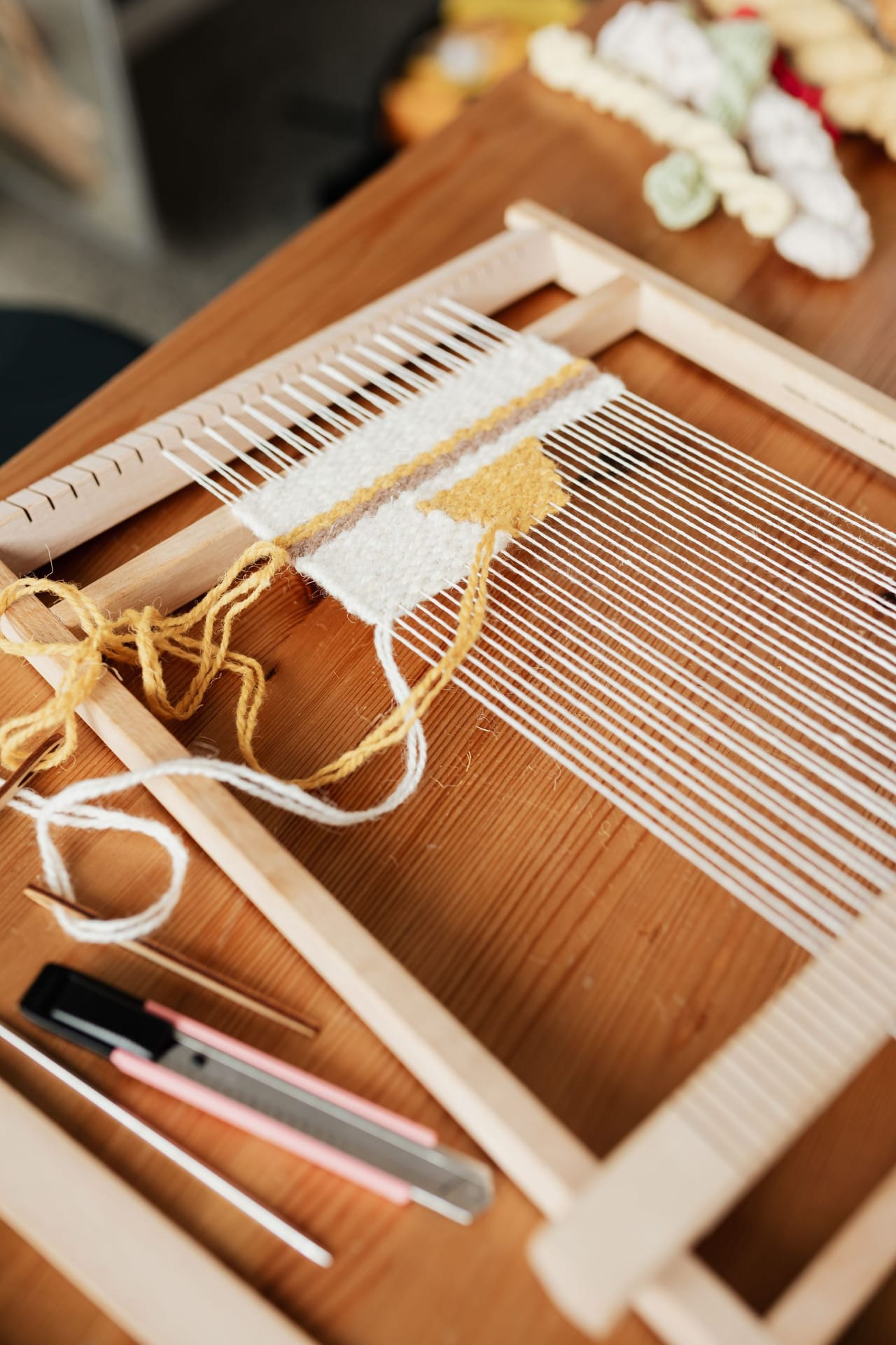 A wooden umbrella yarn swift clamped to a table edge with a skein of yarn stretched around its arms, showing the spoked wheel design that rotates as the yarn winds off