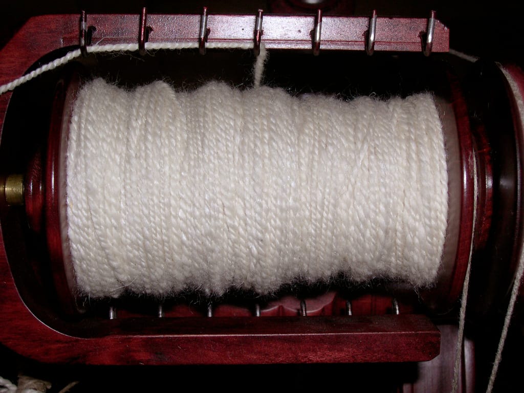 Hands spinning fiber on a drop spindle, showing the kind of handspun yarn that spinners wind into skeins and then off a swift into center-pull balls