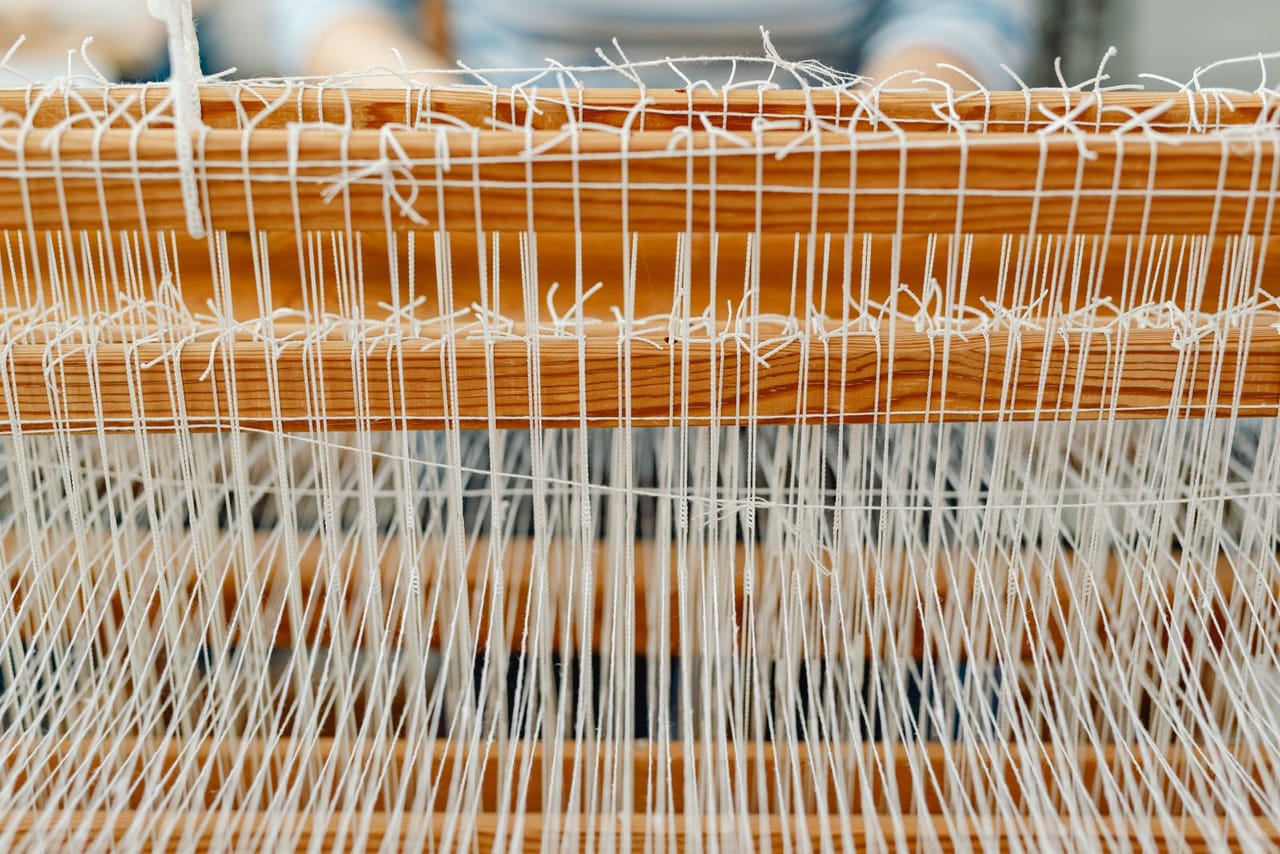 Warp threads under tension on a wooden rigid heddle loom, seen from the front with heddle and reed in frame