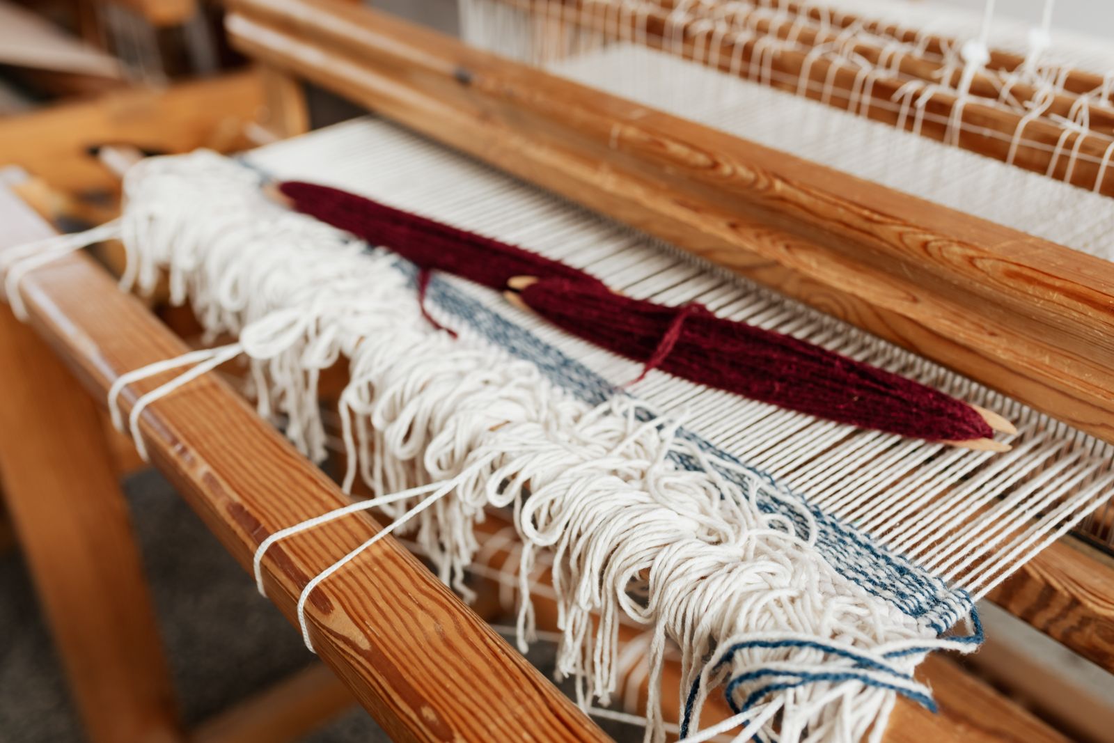 Floor loom in a weaving studio with tensioned warp threads stretched across the frame, shafts and heddles visible in a yarn-filled craft room