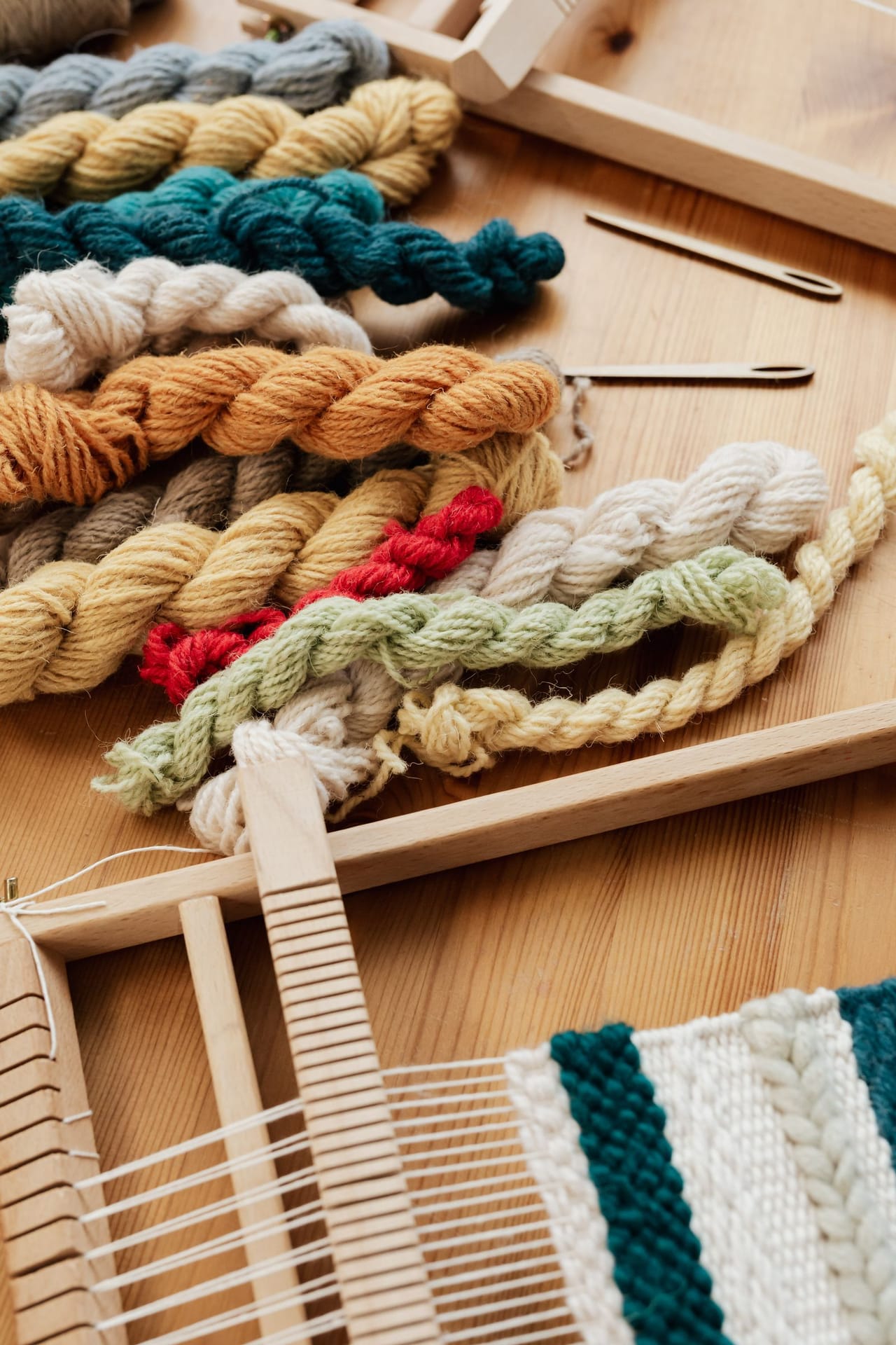 A weaver's hands working colorful yarn on a floor loom, showing warp threads in parallel lines under tension with the shuttle ready to pass