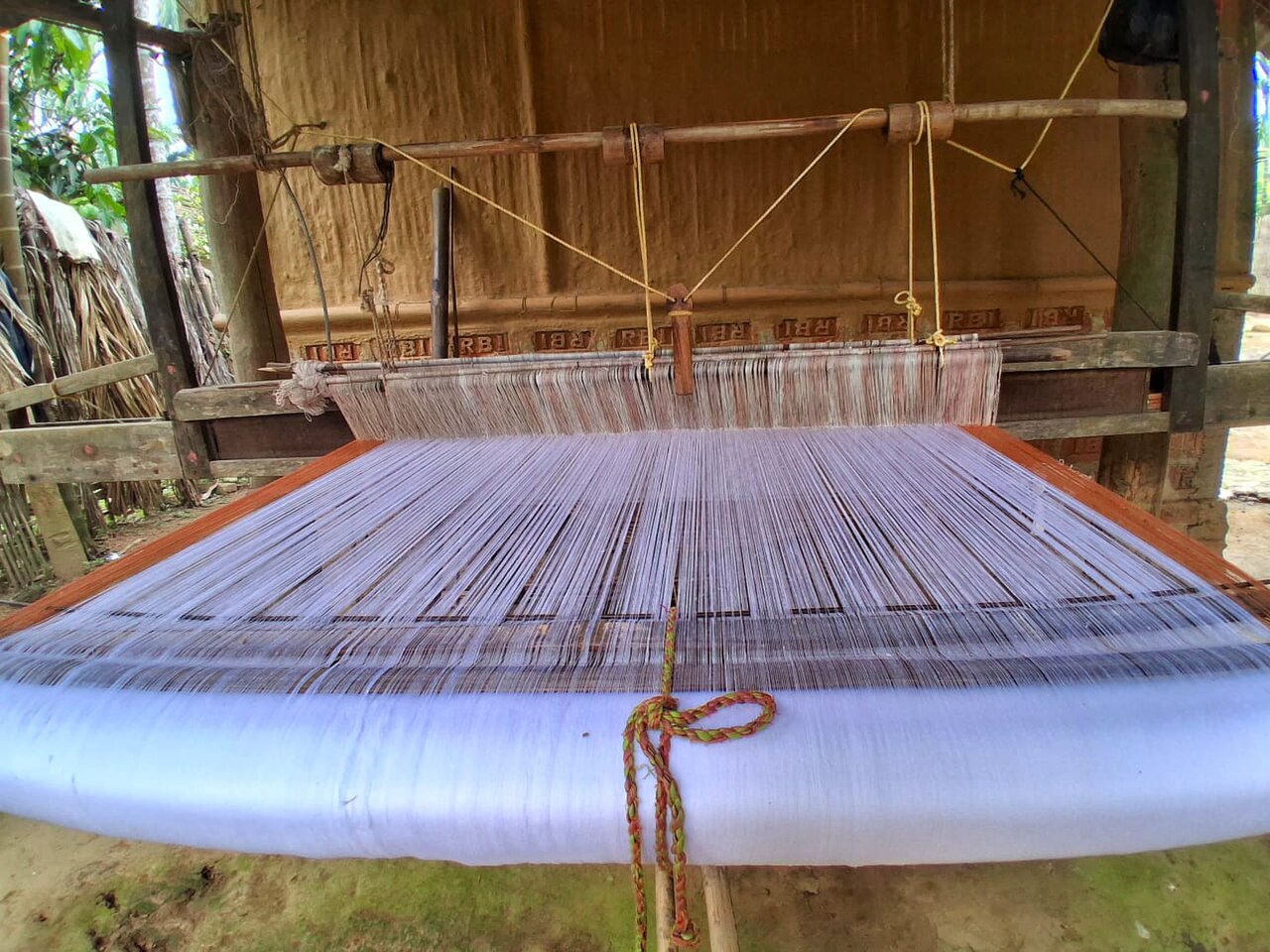 A traditional manual handloom with a heddle and beater, showing the full loom structure from warp beam to cloth beam