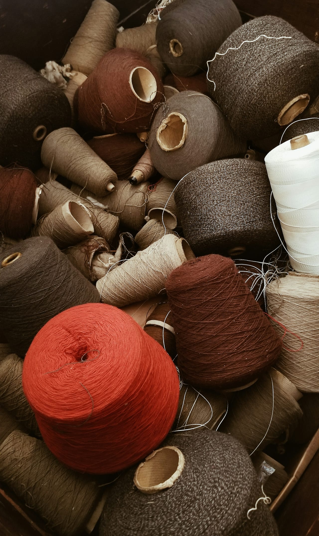 Wooden thread spools and fiber arts materials in a heritage studio setting showing traditional spinning and fiber work materials