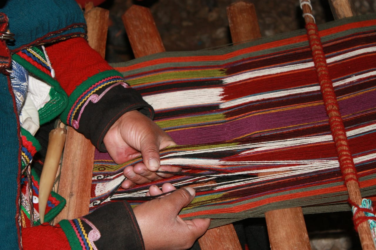Overhead view of a weaver working the weft through a colorful warp on a wooden rigid heddle loom