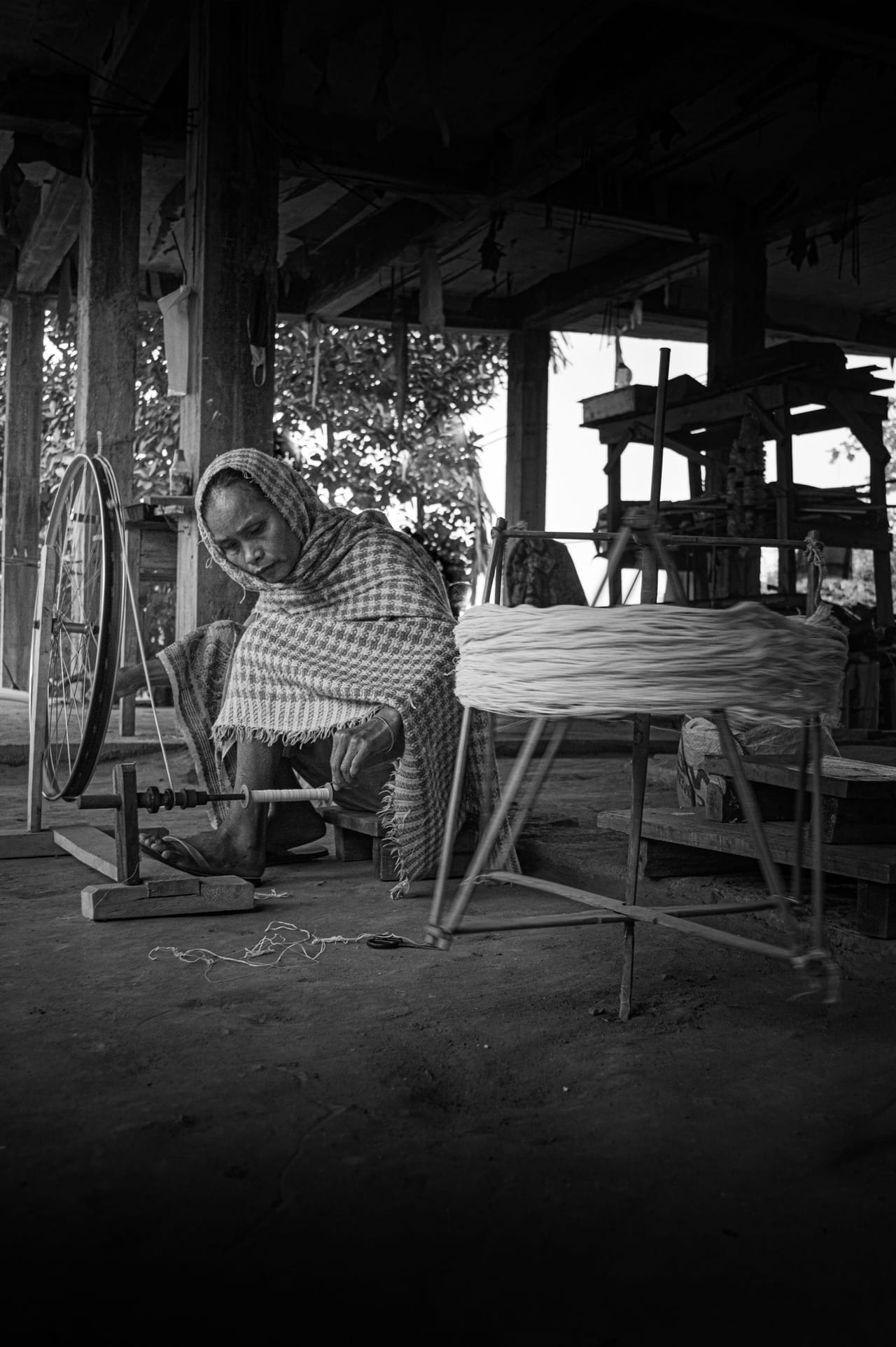 Woman drawing fiber through the orifice of a spinning wheel in a traditional fiber arts workshop, wheel turning during spinning