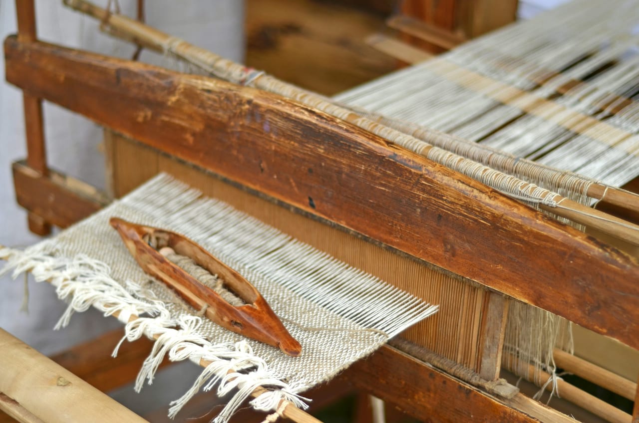 Close-up of an antique weaving machine showing heddle bars, yarn slots, and the worn wood and metal hardware of a traditional textile loom