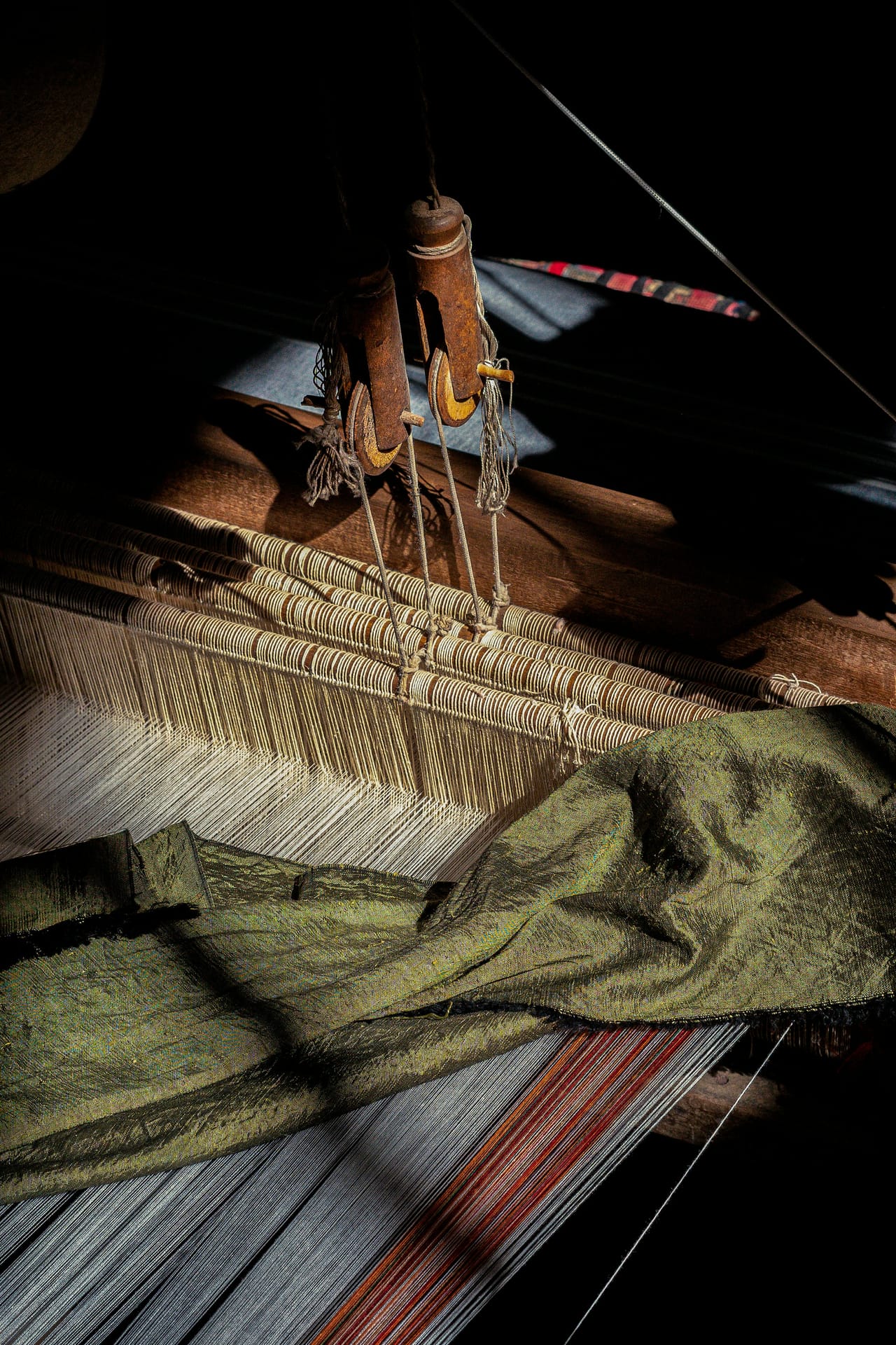 Close up of a traditional weaving machine showing wooden heddles, tensioned warp threads, and the intricate structure of a floor loom in active use