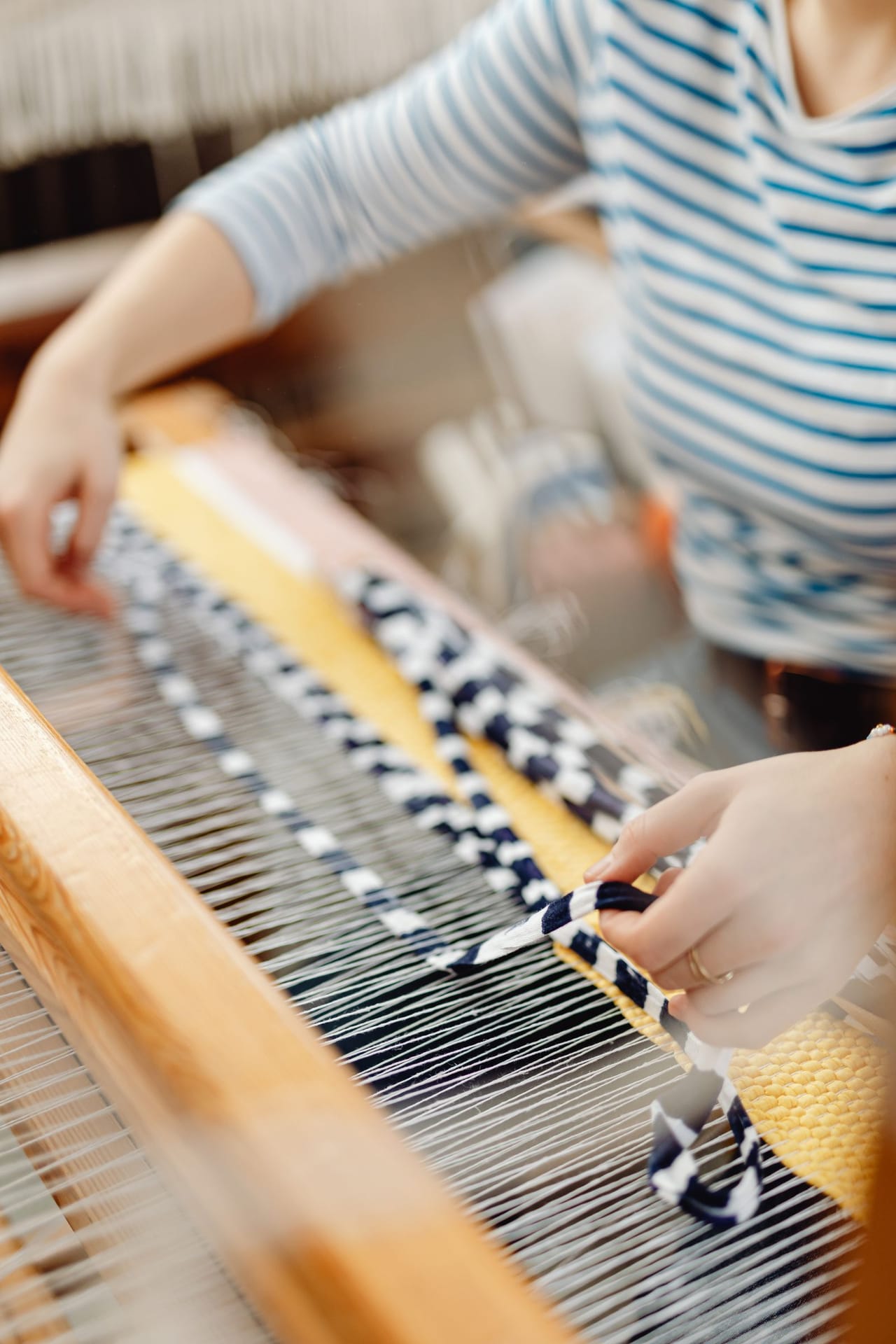 Hands weaving plain weave in cream yarn on a small wooden rigid heddle loom