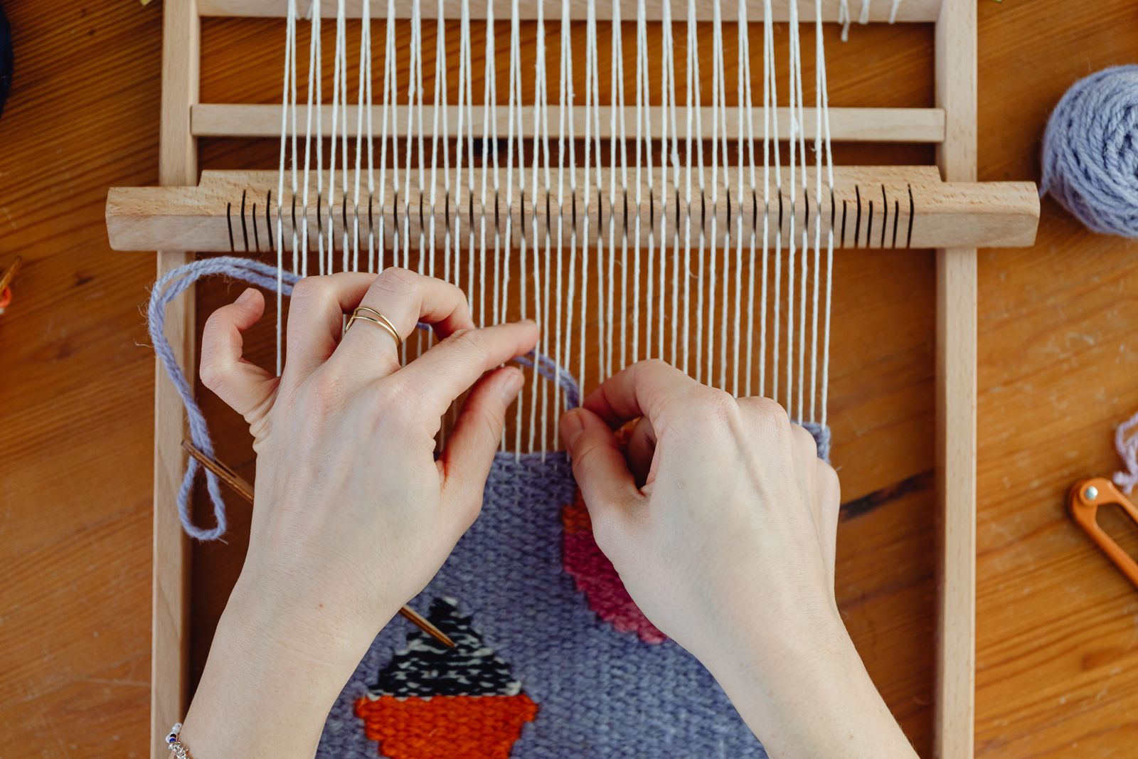Hands beating weft into place on a small wooden rigid heddle loom, woven cloth building up below
