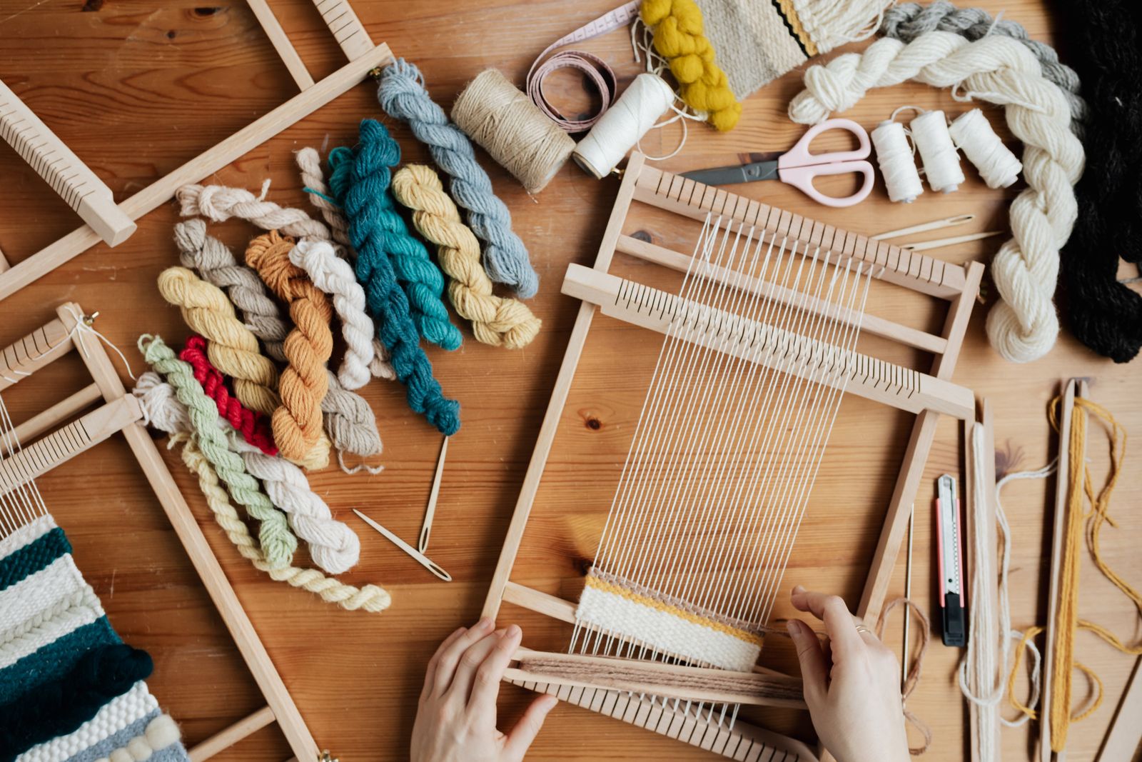 Hands weaving colorful yarn on a floor loom, showing warp threads under tension and the weaving shed formed between raised and lowered warp ends
