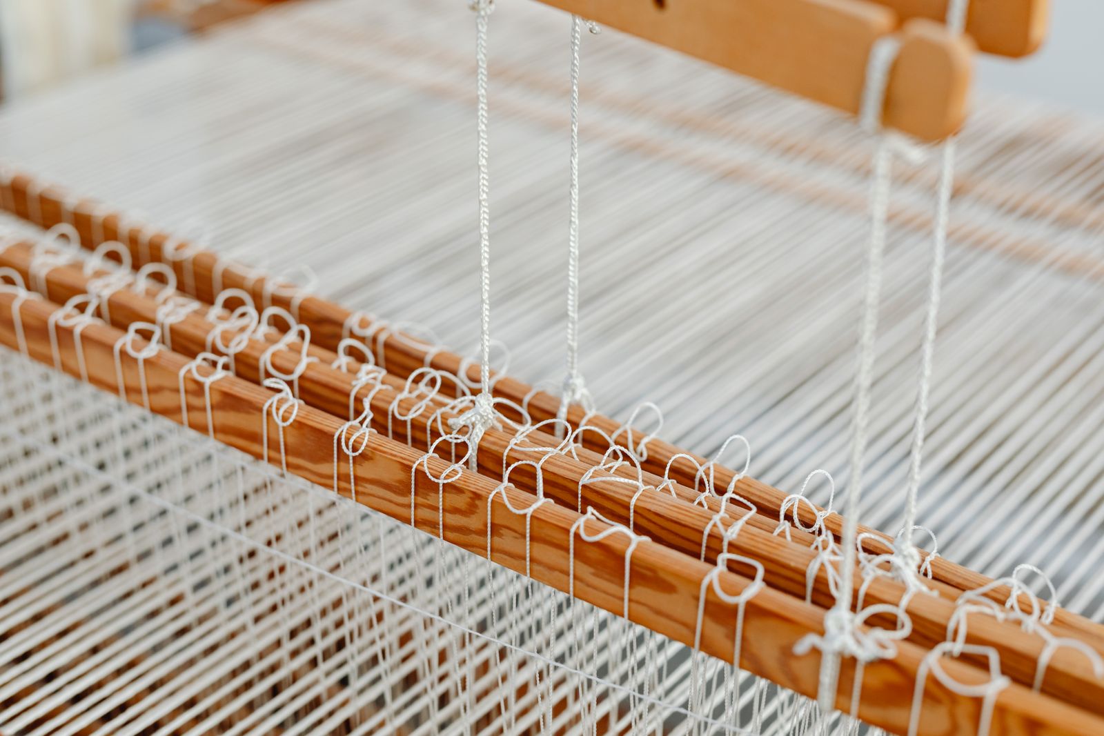 Close-up of a floor loom with tensioned warp threads stretched across the shaft frames and beater showing the loom warped and ready