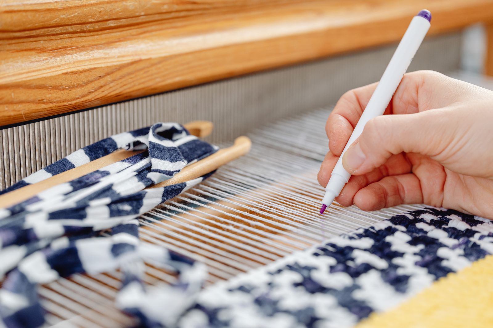 Hands working a rigid heddle across the width of a rigid heddle loom during the weaving process