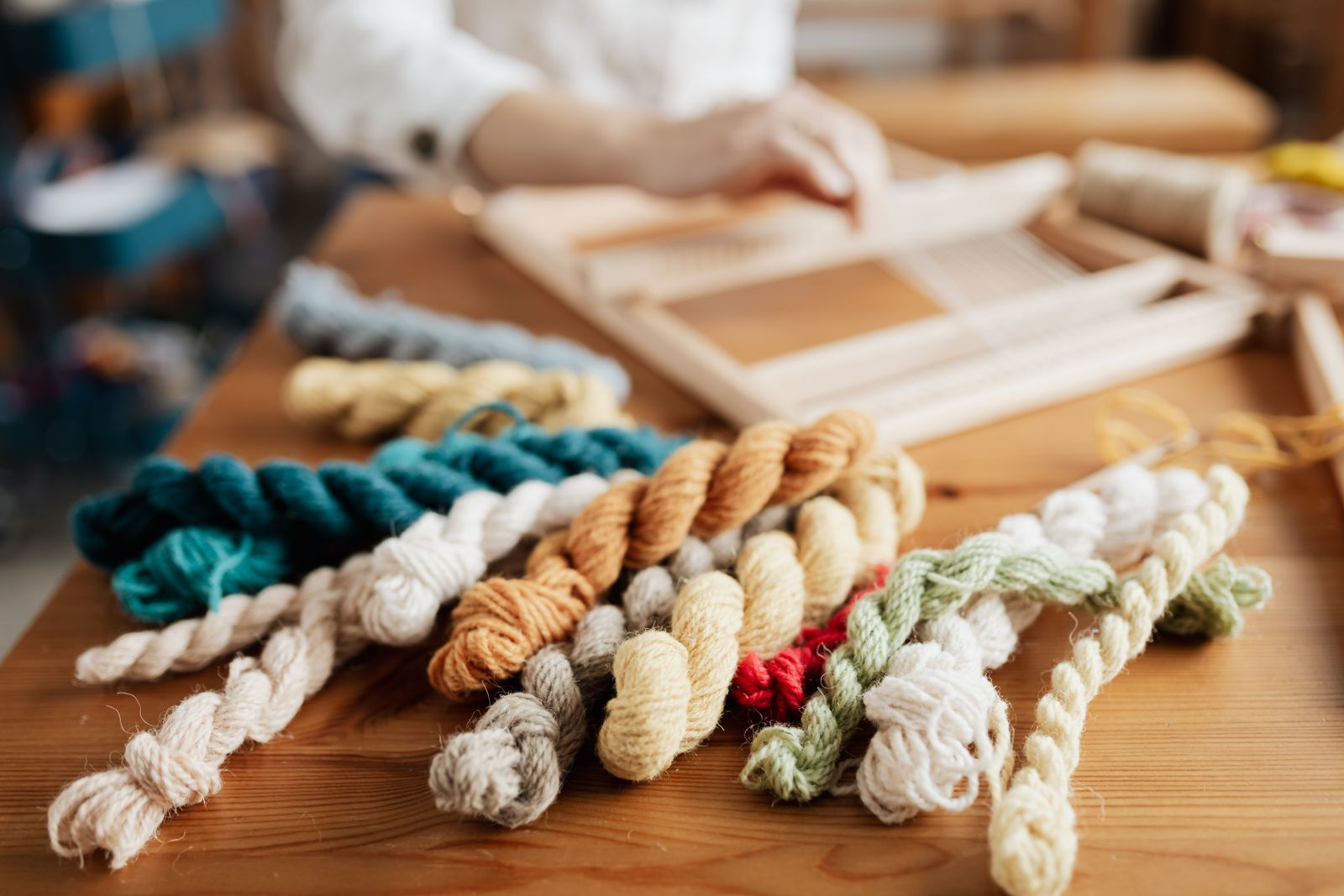 Colorful yarn skeins in various weights and fibers arranged on a wooden table, showing the variety of options available for weaving projects
